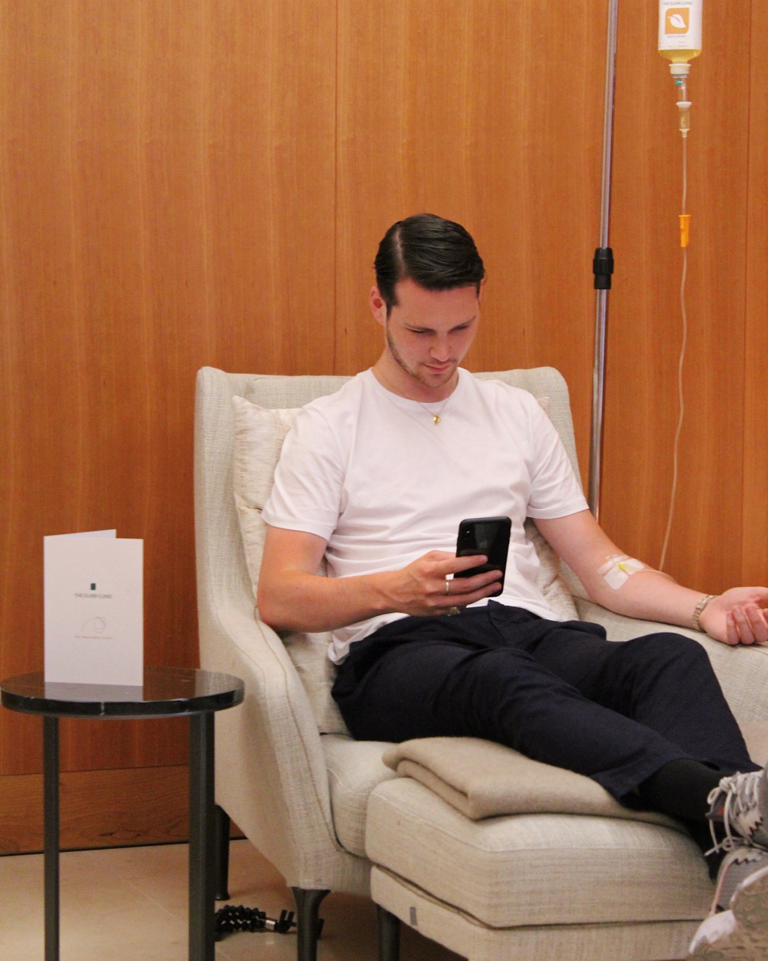 A patient on his phone during an IV drip at The Elixir Clinic